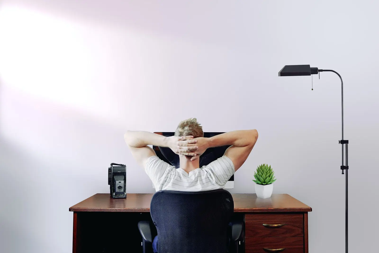 man sitting down holding his head while sitting on chair near computer desk